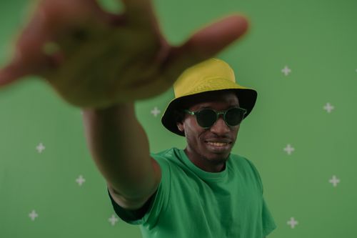Free A man poses confidently on a green background, wearing sunglasses and a hat, exuding a vibrant and stylish vibe. Stock Photo