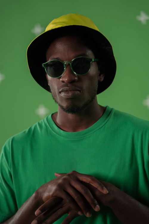 Free Studio portrait of a man wearing sunglasses and a bucket hat against a green background. Stock Photo
