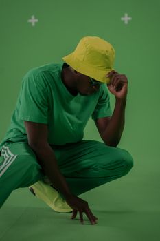 Stylish man posing in vibrant green studio wearing matching attire and yellow hat.