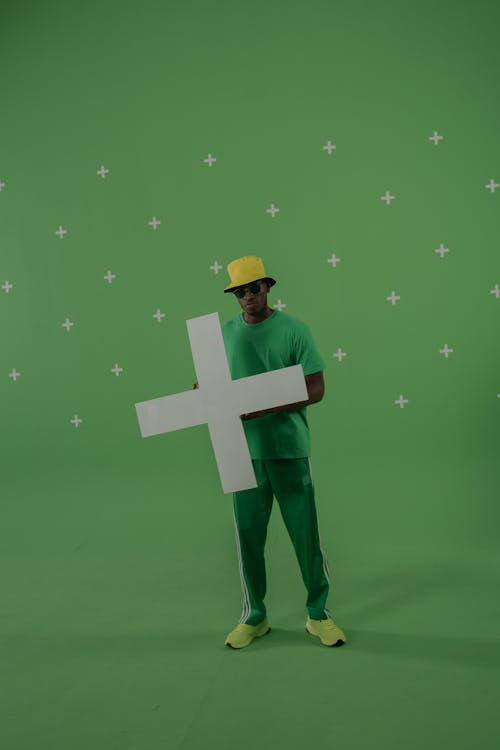 A Man in a Green Attire Holding a Cross Cutout