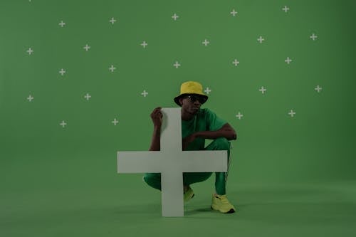 Man with Yellow Hat Crouching by Plus Symbol in Studio