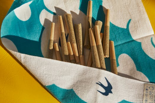Collection of cannabis joints on blue and white patterned fabric, sunny setting.