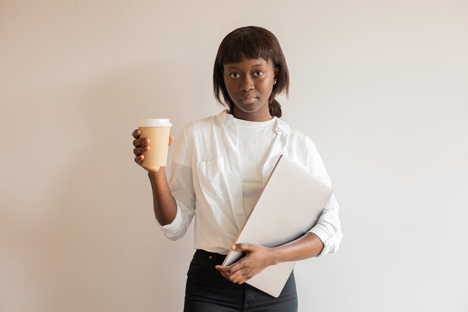 Professional woman holding disposable cup and laptop in medium close-up indoors.