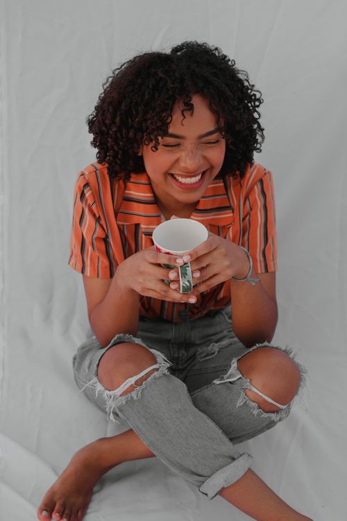 Free Joyful woman sitting indoors holding a cup, radiating warmth and happiness. Stock Photo