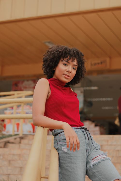 Free Confident young woman with curly hair posing in a sleeveless top, leaning on a railing outdoors. Stock Photo