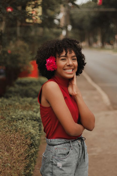 Free A cheerful woman with a pink flower in her hair, posing outdoors in a vibrant setting. Stock Photo