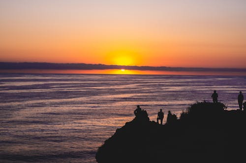 Silhouette of People on the Rocky Coastline near Ocean during Sunset