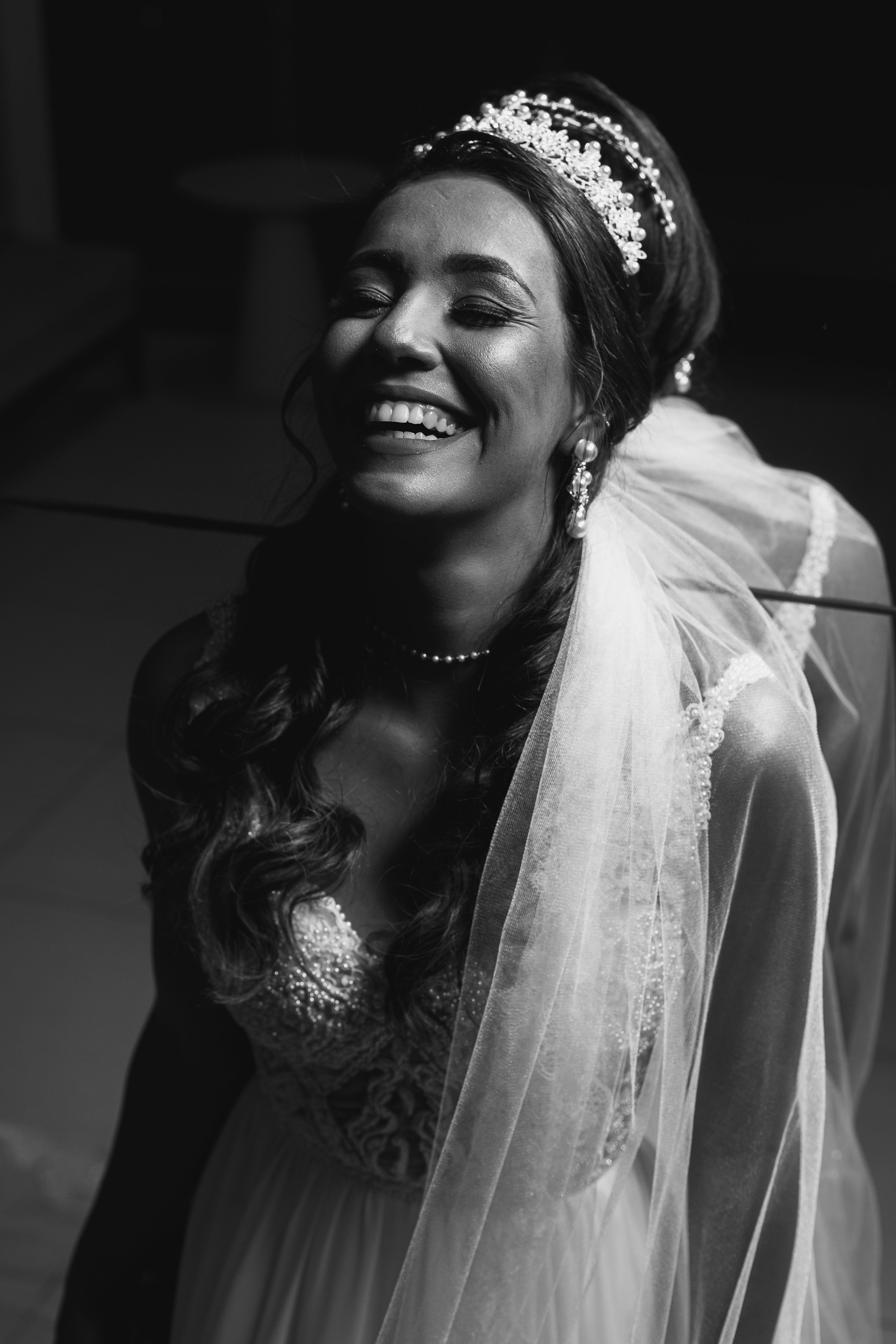 A joyful bride in elegant attire smiling while looking in the mirror, captured in black and white.