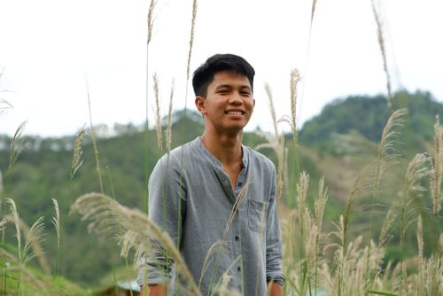 Free Portrait of a smiling man standing in a grassy field with mountainous backdrop. Stock Photo