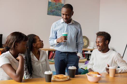 Four colleagues having a casual coffee break with snacks in an office setting, fostering teamwork.