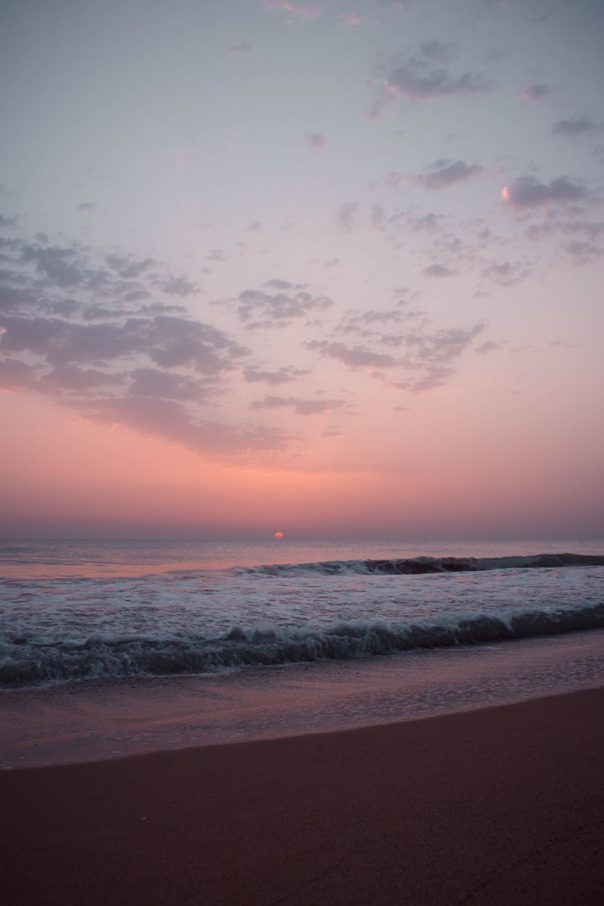 Peaceful beach scene with gentle waves under a pastel-hued sunset sky.