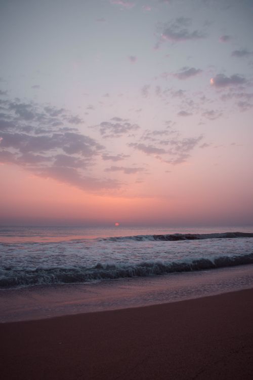 Free Peaceful beach scene with gentle waves under a pastel-hued sunset sky. Stock Photo