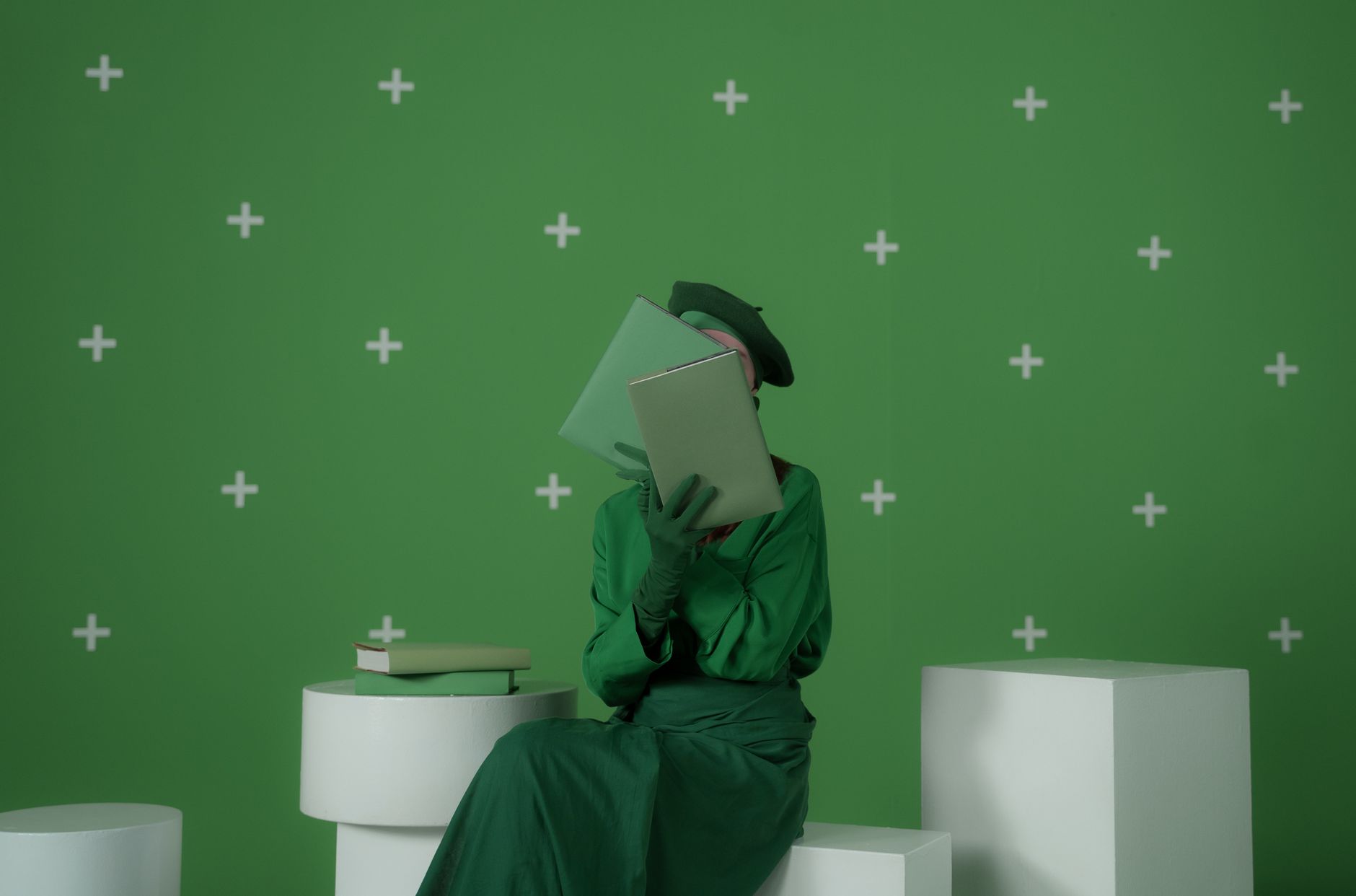 A woman in a green outfit sits reading a book against a chroma key green backdrop.