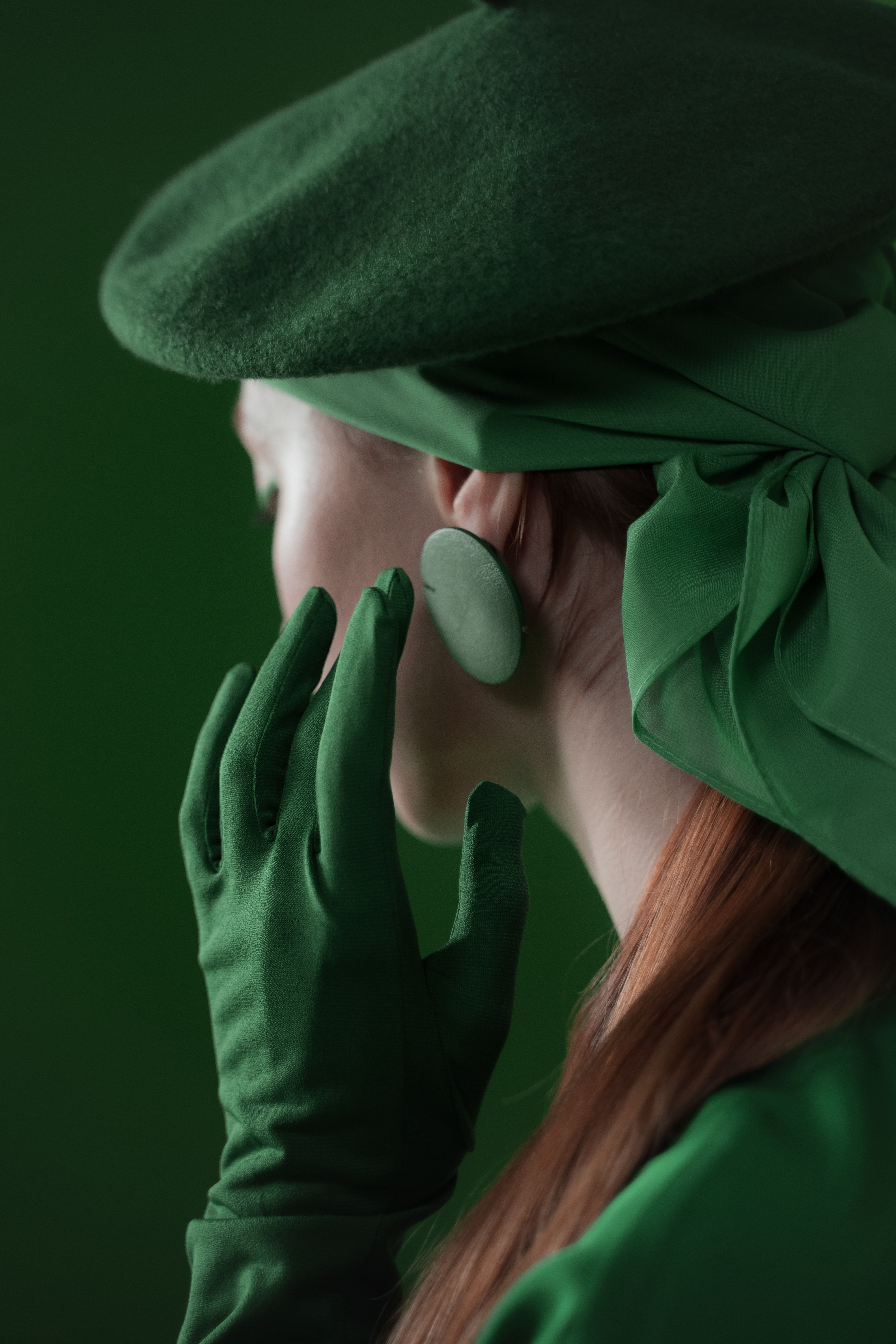 Close-up of a woman in a stylish green outfit with gloves and hat, viewed from behind.