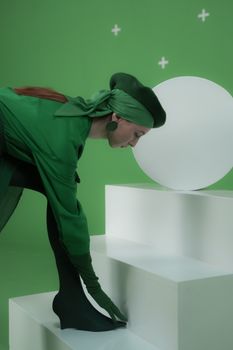 Surreal fashion portrait of a woman in green posing on white steps in studio.