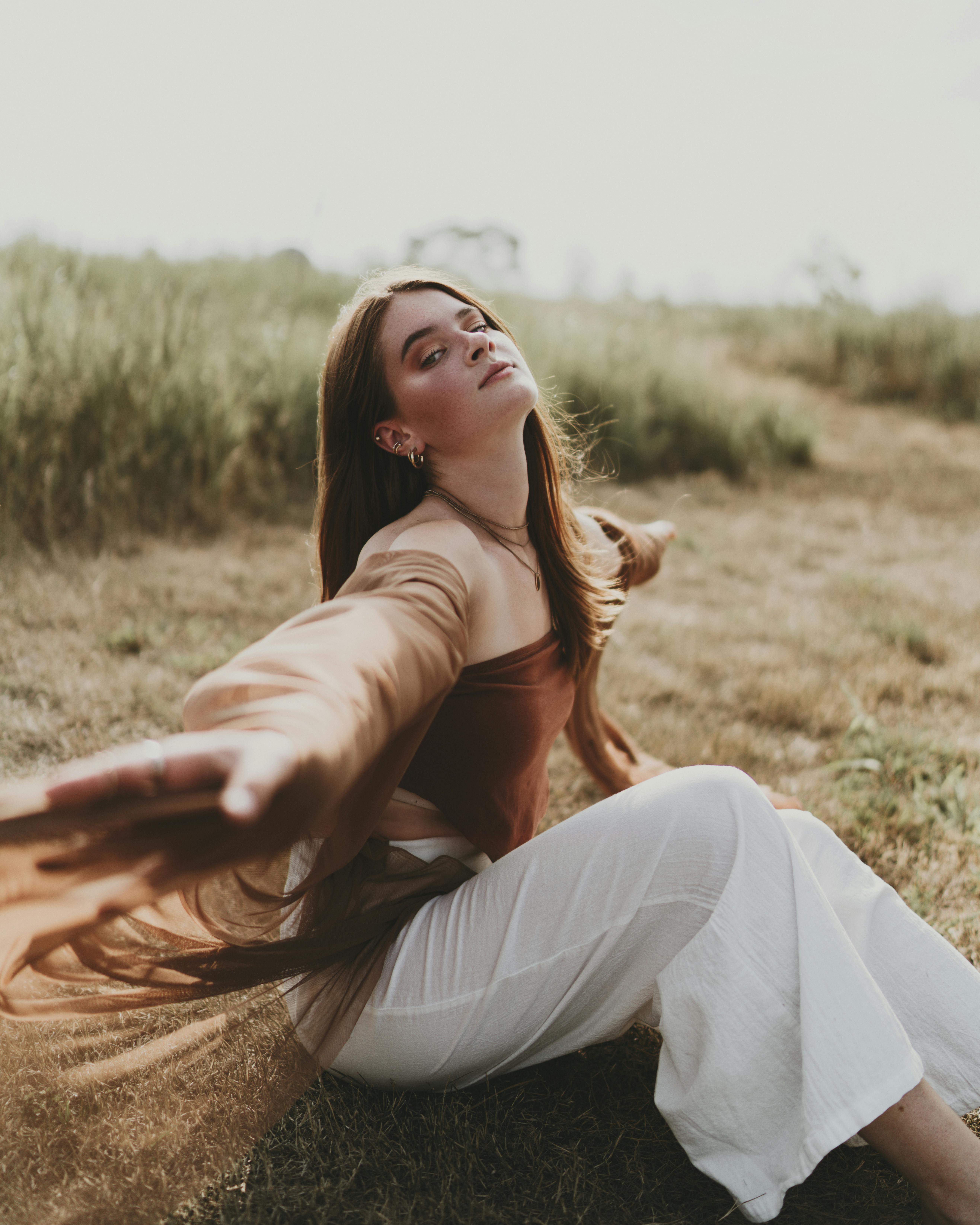 fashion girl sitting on grass in meadow with hands stretched out