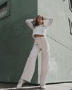 Woman in White Long Sleeve Shirt and White Pants Leaning on Green Wall