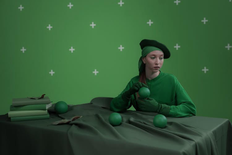 A Woman In Green Outfit Holding Green Round Object On A Green Background