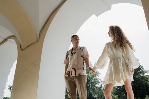 Free A couple holding hands under an elegant archway, showcasing intimacy and love. Stock Photo
