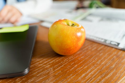 A ripe apple sits on a wooden desk beside a laptop, conveying a healthy work environment.
