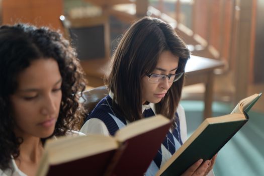 Two female students reading books in an educational setting. Perfect for school and study themes.