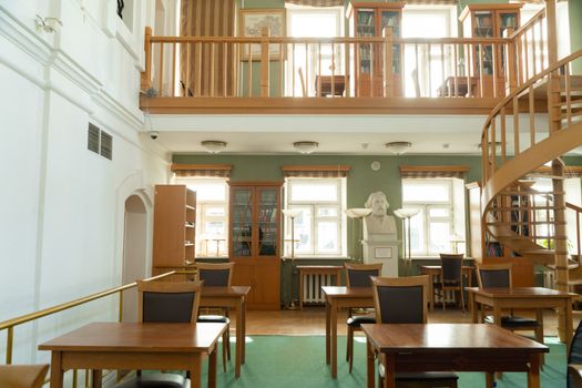 Spacious library interior featuring wooden tables and spiral staircase under natural light.