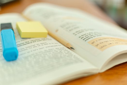 Close-up of an open book with a highlighter and sticky notes for study reference.