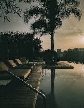 A serene and luxurious tropical poolside scene with sun loungers at sunset.