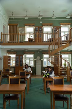 A serene library interior featuring wooden furniture, books, and a spiral staircase.