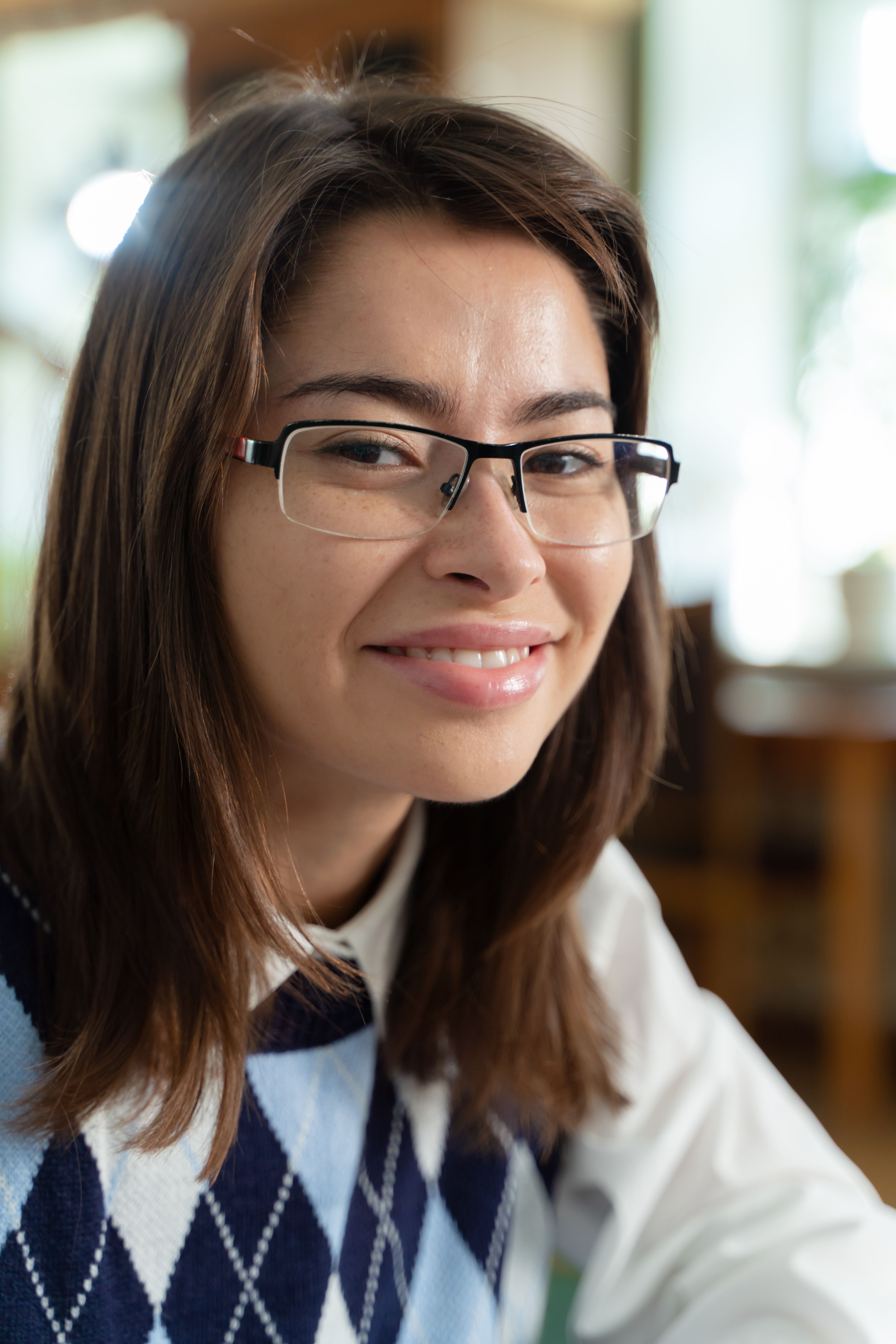 Portrait of a smiling woman wearing glasses indoors, exuding warmth and friendliness.