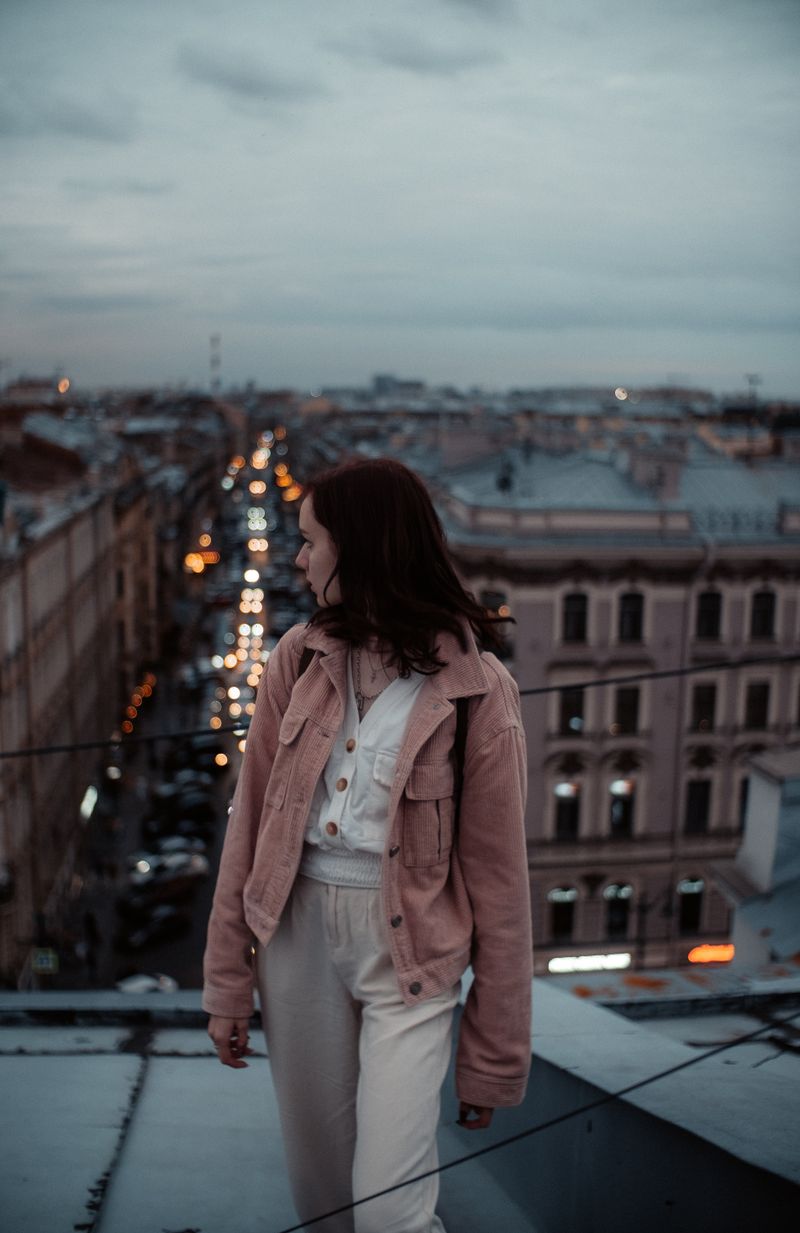A woman standing on a rooftop overlooking a city at dusk — photo by Vitaliy Mitrofanenko on Pexels