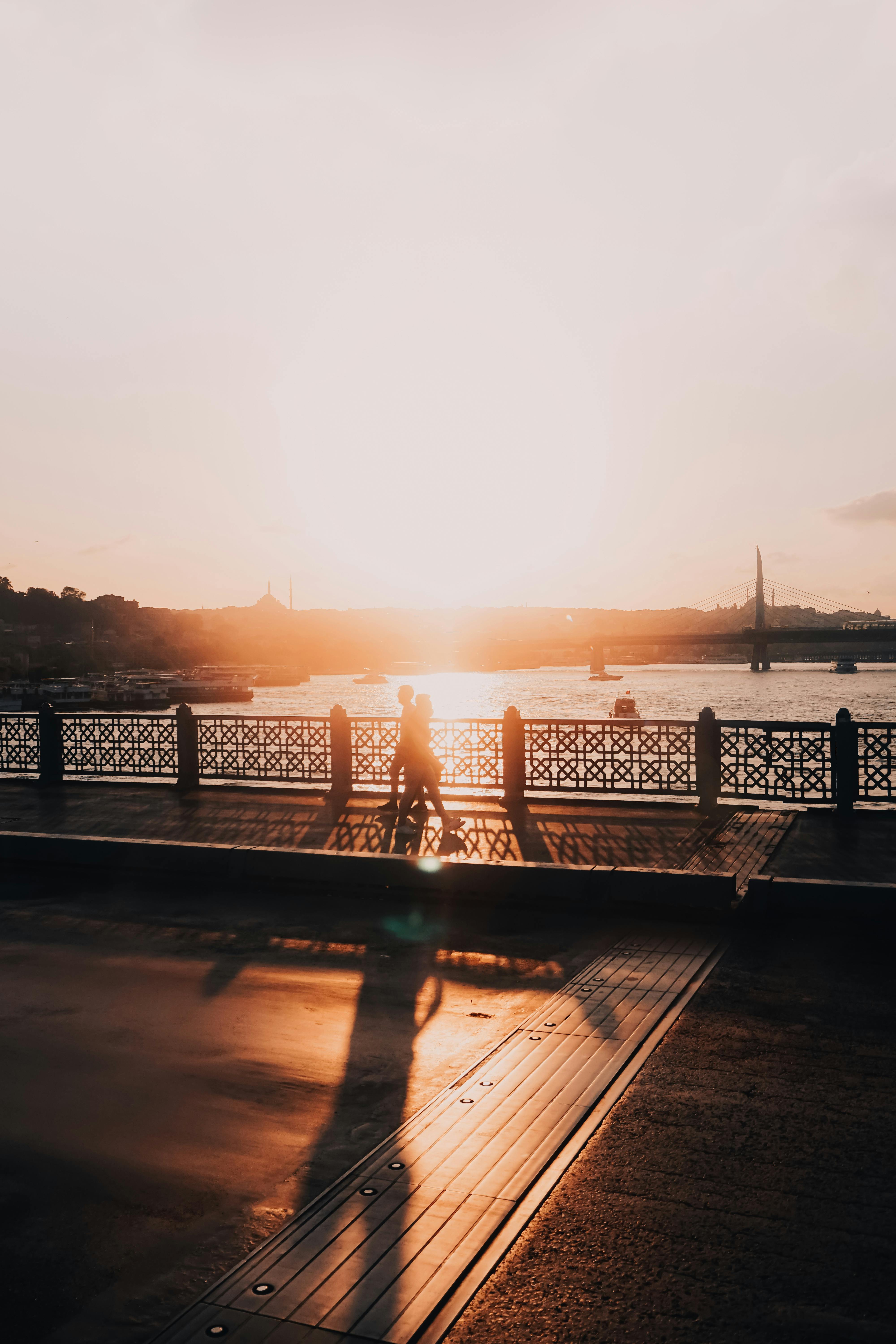 Silhouette of a person walking on a bridge in Istanbul at sunset, overlooking the water and city skyline.