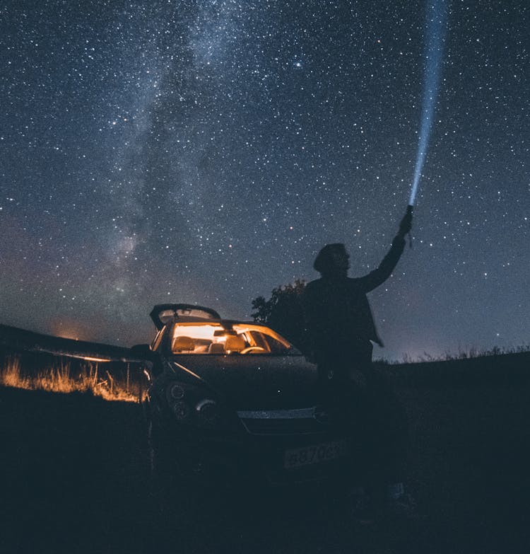 Man Sitting On The Car Hood Under A Starry Night Sky 