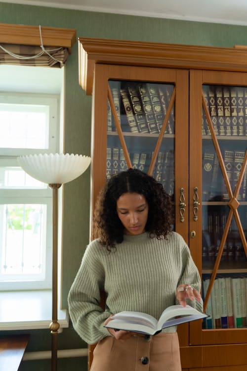 Free Young Woman Standing in a Library and Reading a Book  Stock Photo
