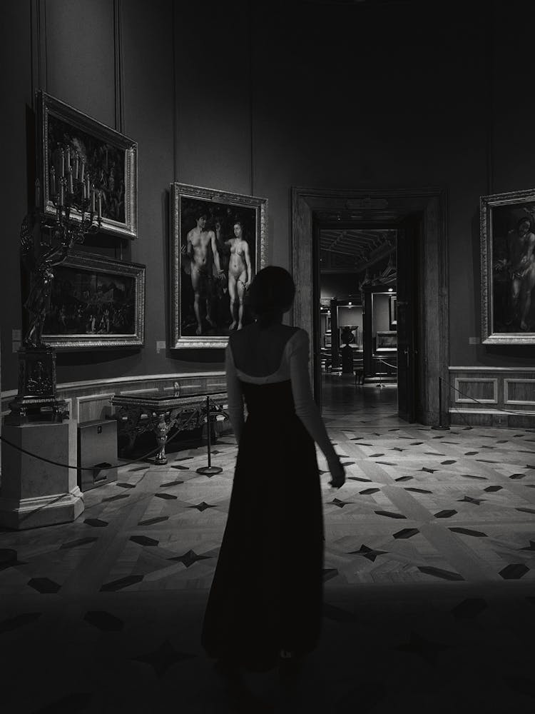 Unrecognizable Woman In Long Dress Walking In Art Gallery By Night