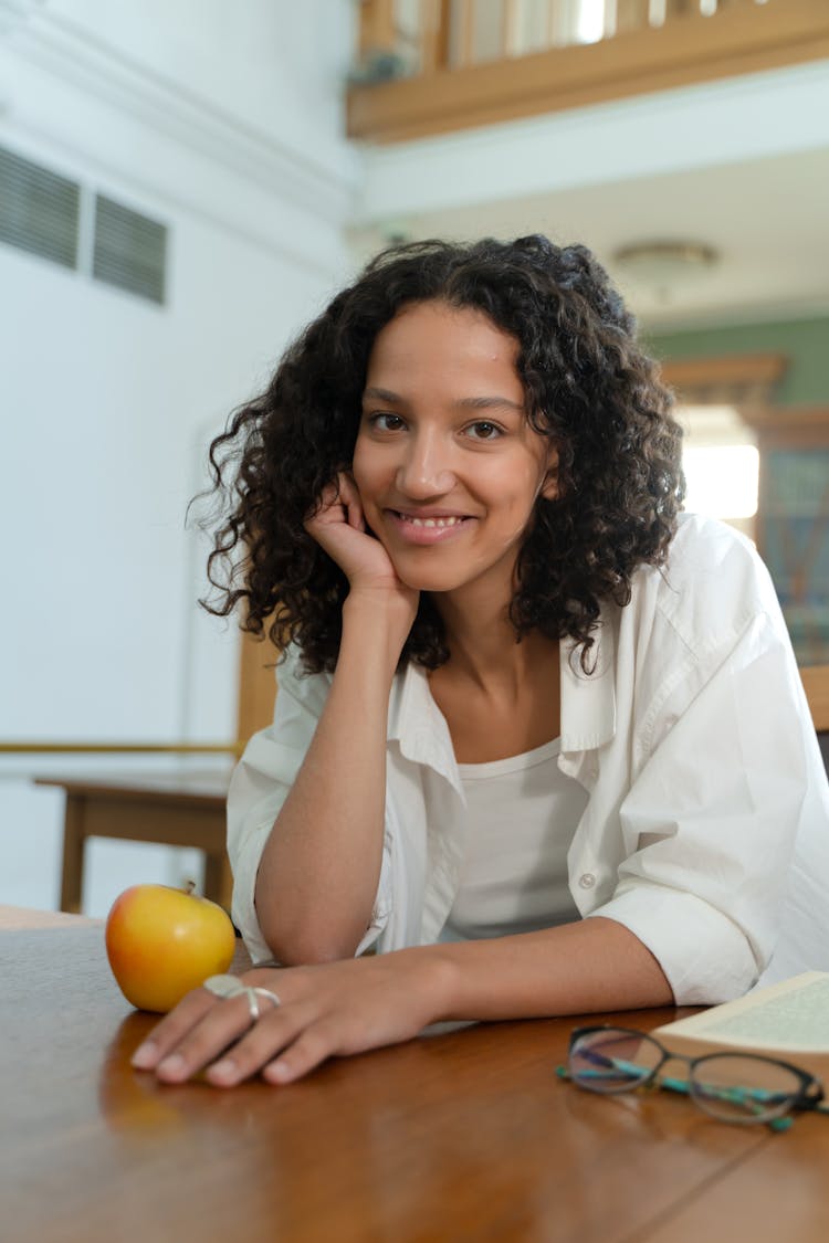 Pretty Student In White Shirt Sitting At Desk In Library