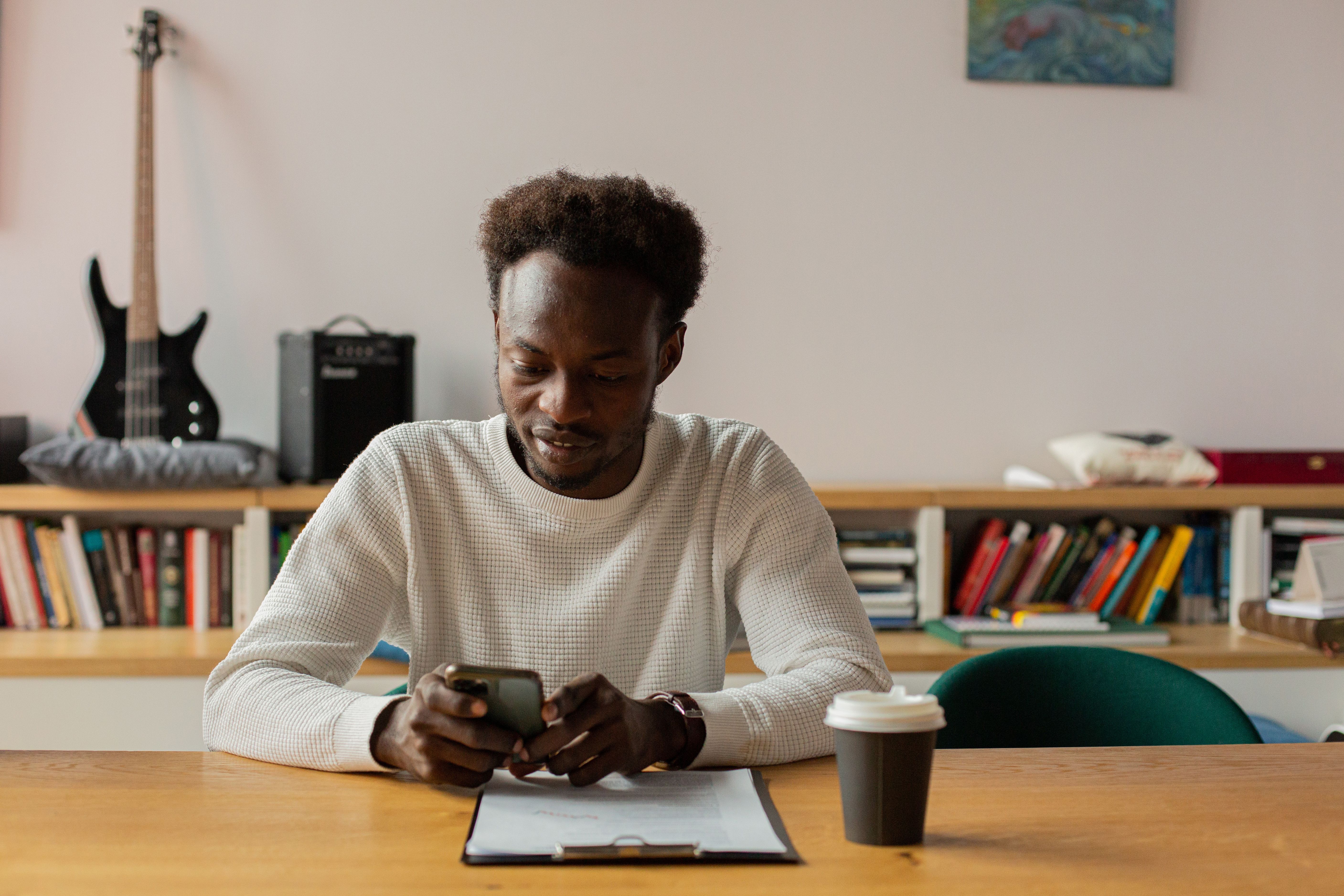 A person sitting at a cluttered desk at 2 PM, looking tired and distracted, with a coffee cup and a phone glowing