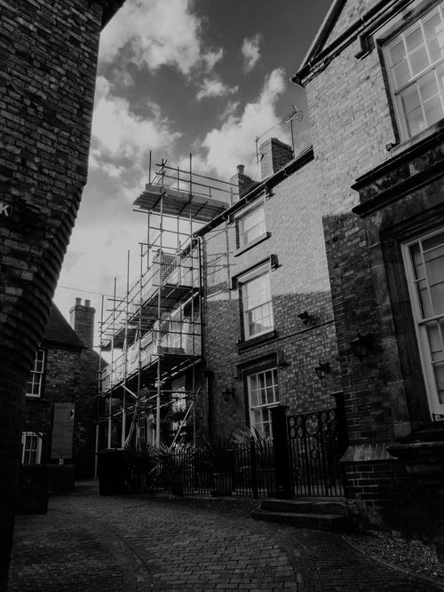 Free Black and white photo of scaffolding on historical brick buildings, highlighting texture and architecture. Stock Photo