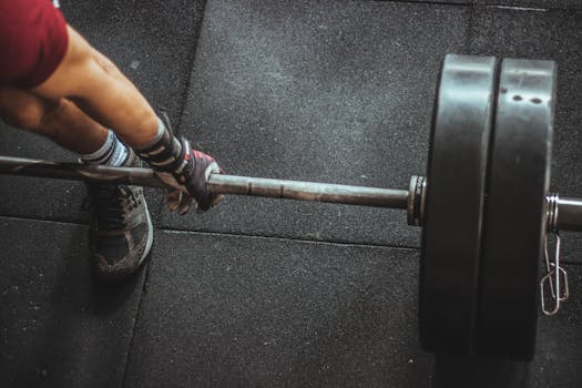Close-up of muscular arm lifting barbell in gym, showcasing strength and fitness.