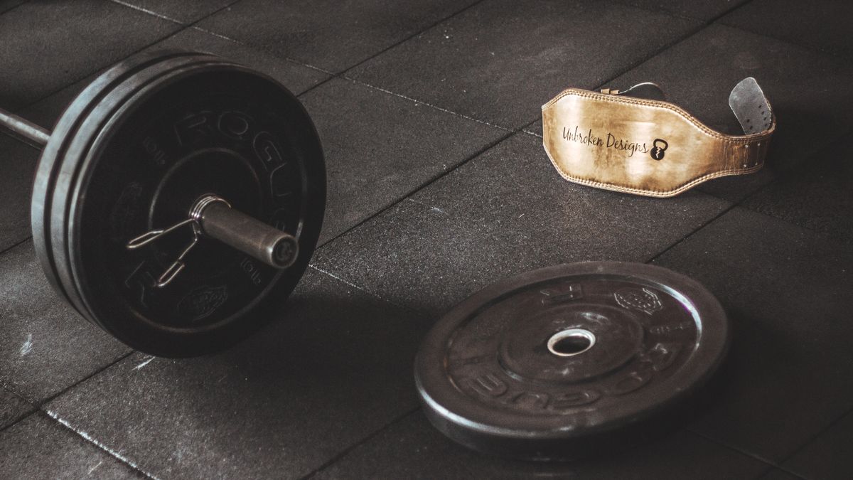 A heavy barbell and weightlifting belt on a gym floor, emphasizing strength and fitness.