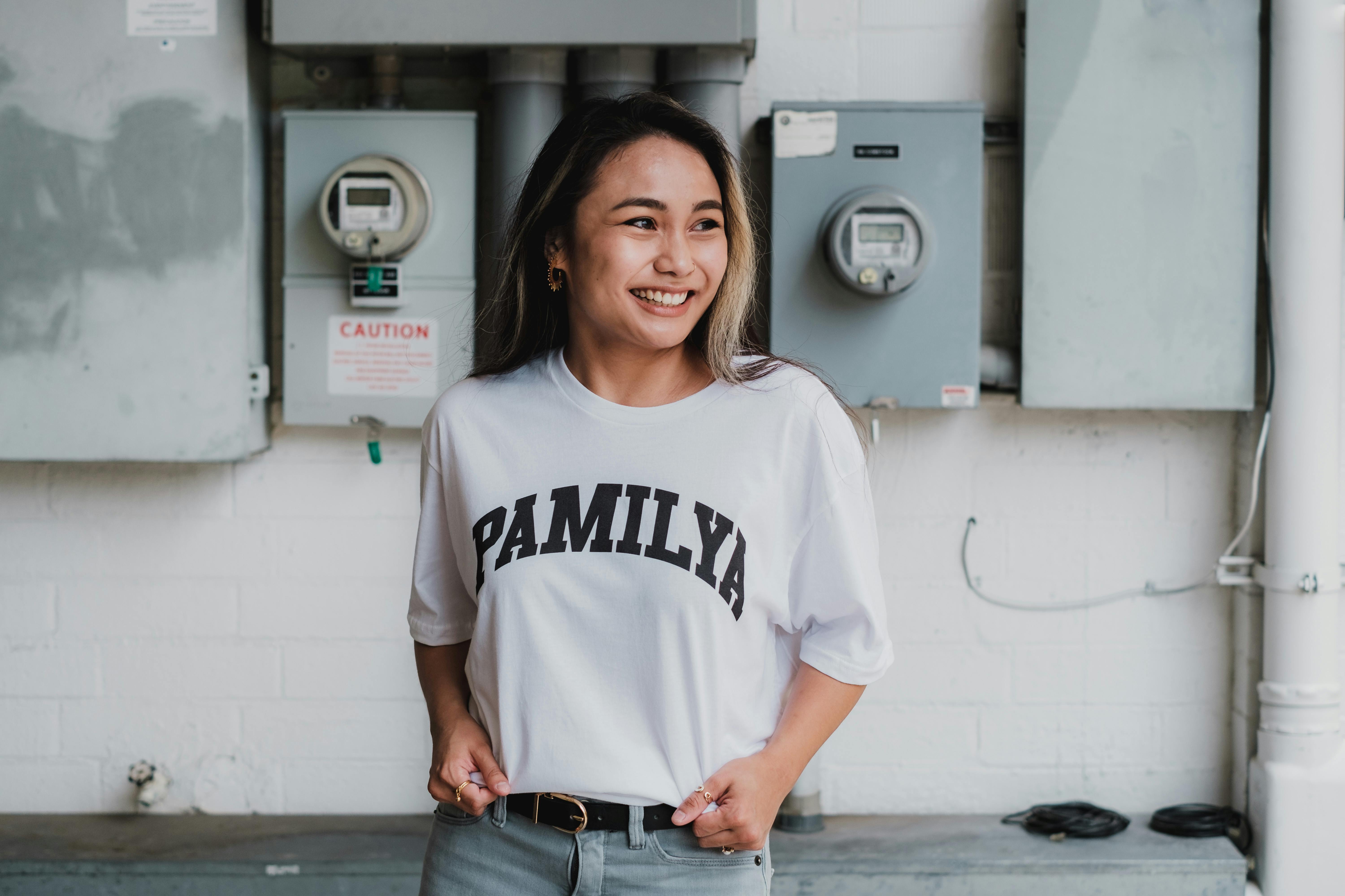 Cheerful woman wearing a 'Pamilya' t-shirt, posing indoors against a neutral background.