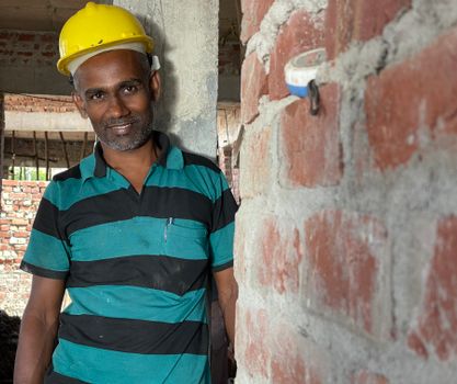 Construction worker in a hard hat smiling by a brick wall indoors.