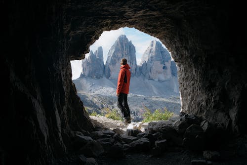 Free Homme En Veste Rouge Debout à L'extérieur De La Grotte En Face De Trois Montagnes Stock Photo