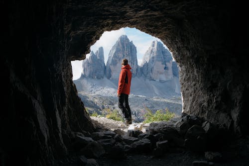 Homme En Veste Rouge Debout à L'extérieur De La Grotte En Face De Trois Montagnes