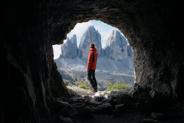 Man In Red Jacket Standing Outside Of The Cave Across The Three Mountains