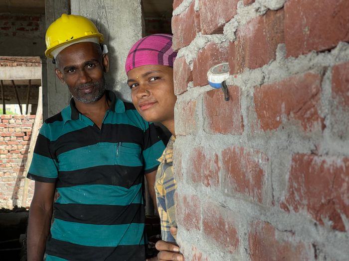 Two construction workers posing with smiles on a brick building site in India