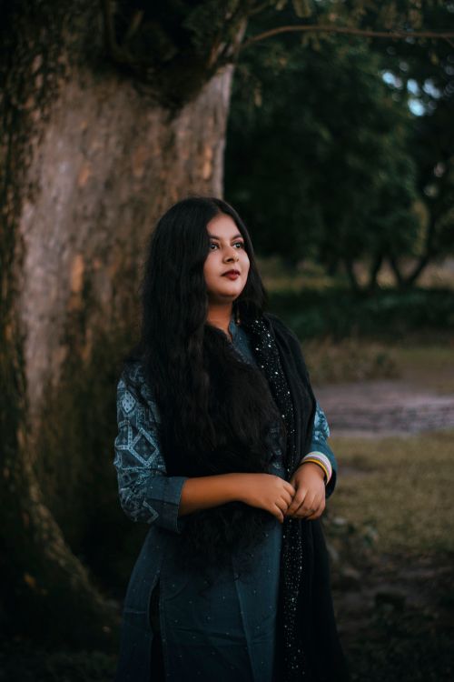 Free Portrait of a woman in traditional attire standing beside a large tree outdoors. Stock Photo