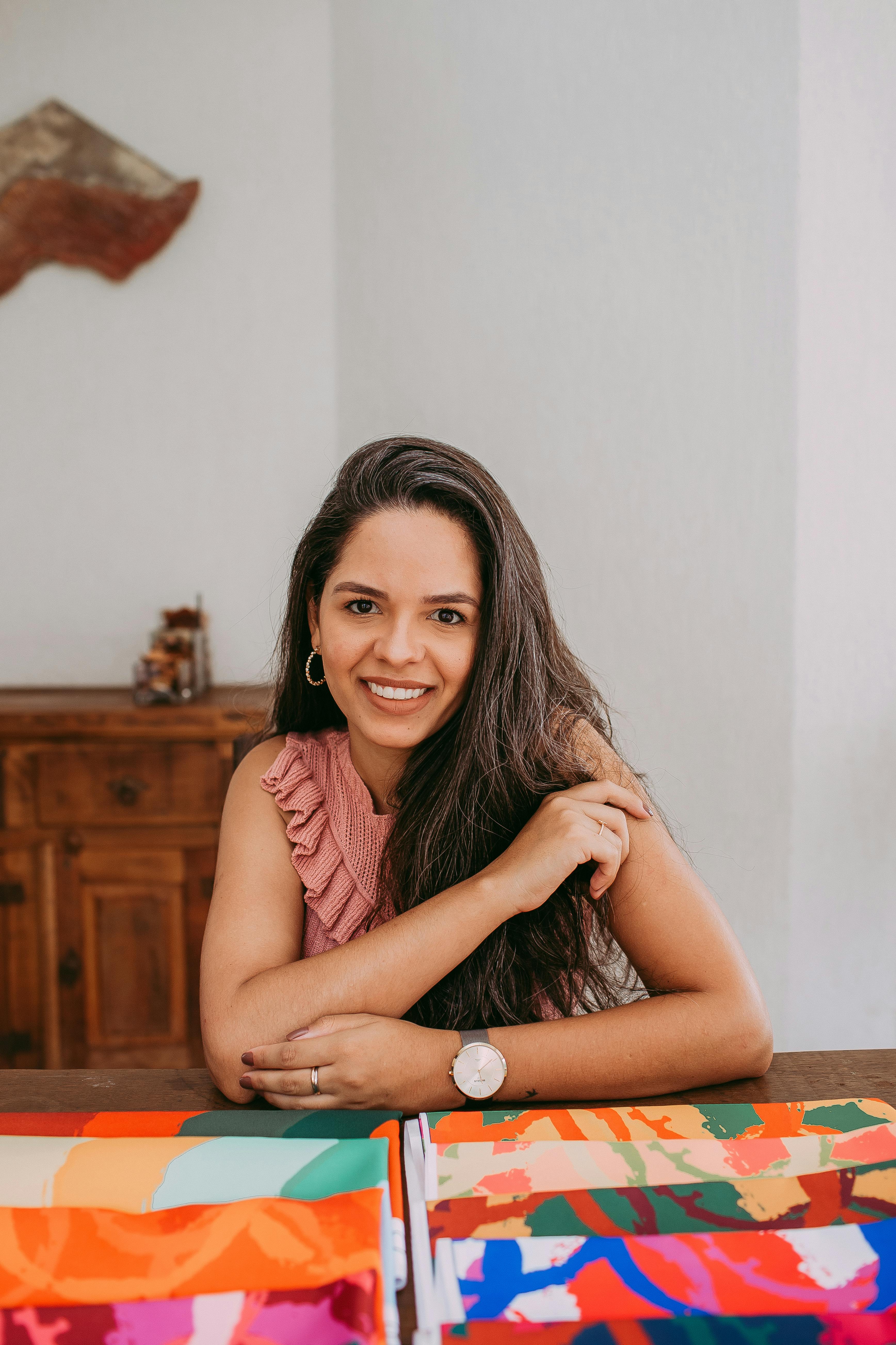 Portrait of a woman surrounded by colorful fabrics, smiling warmly indoors.