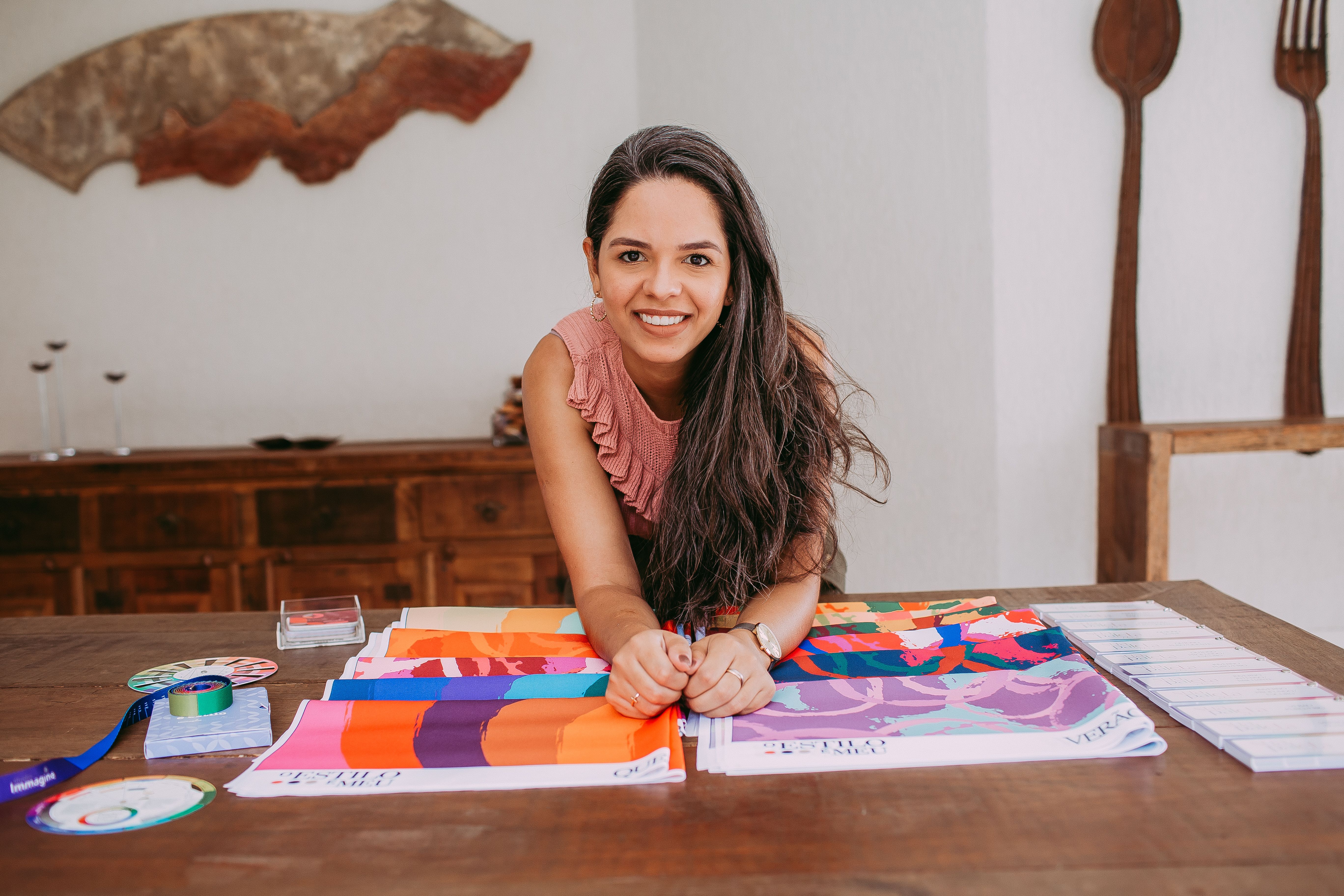 Smiling woman showcasing vibrant fabric samples on a wooden table indoors.