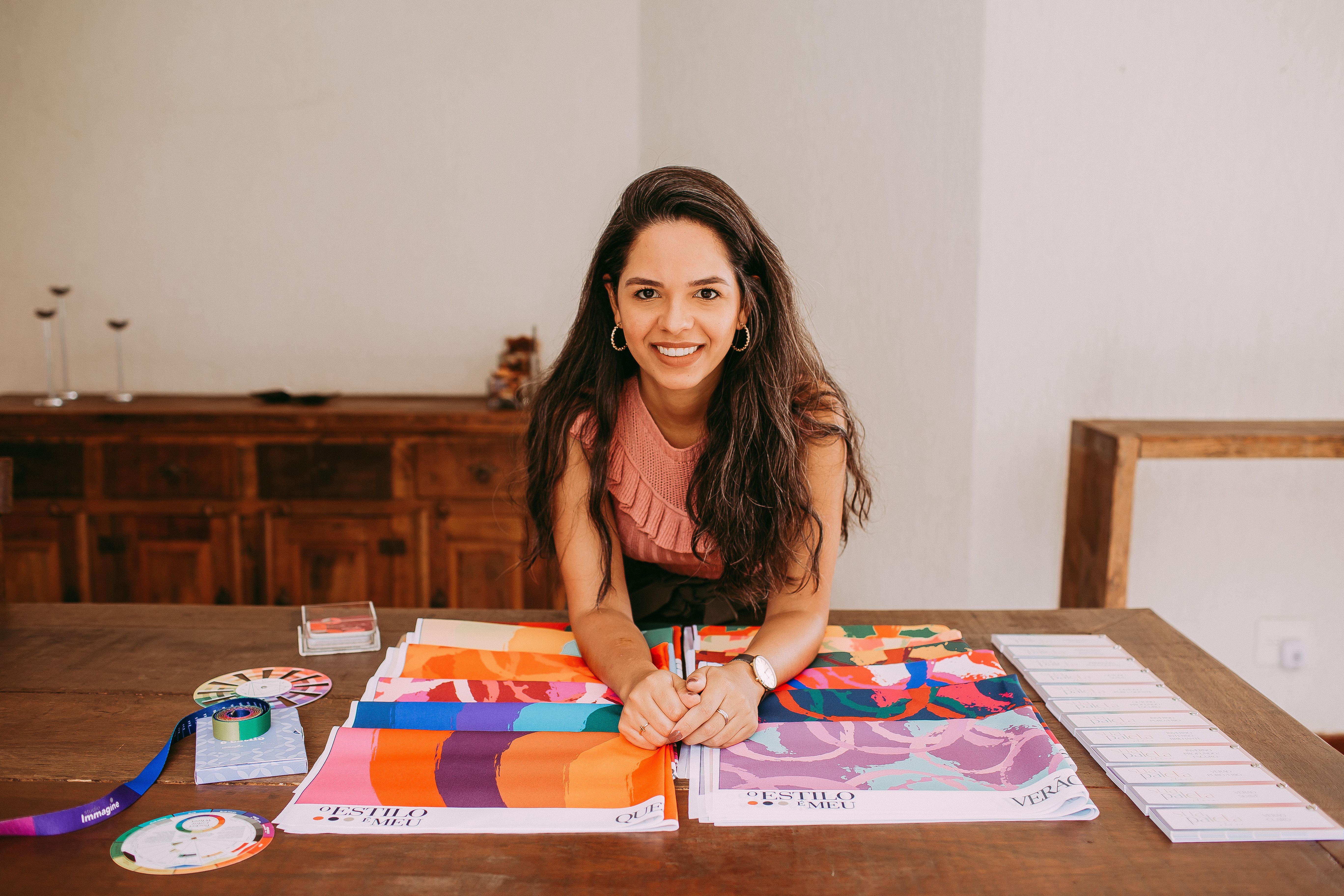 A smiling woman showcasing vibrant fabric samples on a wooden table in a stylish setting.